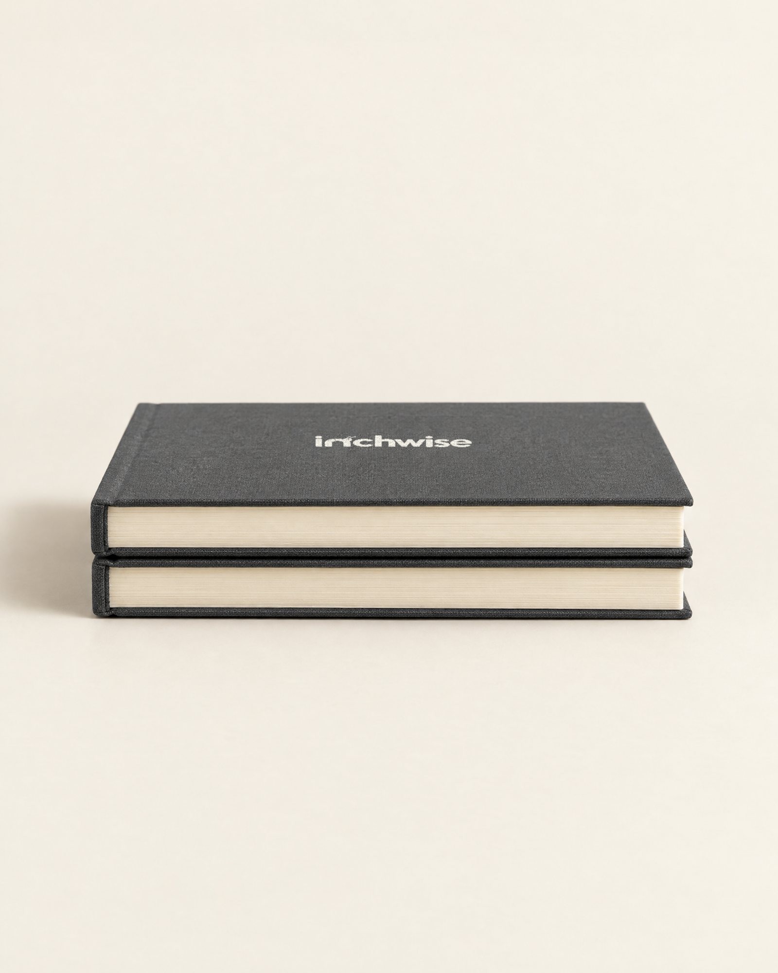 Two Inchwise journals stacked, showing the charcoal cover and cream page edges